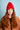 Person wearing a red beanie and brown jacket against a light blue background
