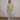 A model stands in a studio wearing a short-sleeve crewneck t-shirt with a geometric pattern in olive green, beige, and taupe, paired with wide-leg light-wash jeans and brown leather loafers.