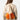 A model wearing an orange and cream colored backpack on a white background. 