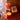 An orange candle holder with candle burning on wood surface. 