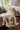 A patterned knit throw blanket draped over a sofa in a living room setting. The blanket features an abstract, organic pattern in olive green, lavender purple, mustard yellow, and cream.