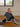 Woman sitting on a wooden floor in a room with large windows.