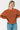 A woman wearing a chunky orange ribbed knit sweater and blue jeans, posing against a plain white background.