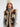 Handknit vest with horse motif and faux fur lining worn over a grey turtleneck paired with brown plaid pants on white background.