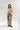 A model stands against a light gray studio background wearing a cream fuzzy cropped sweater with fringe and embroidered detailing, loose patterned gray pants, and brown slip-on shoes.