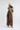 A model stands against a light gray studio background wearing a cream knit beanie, a gray turtleneck, a brown patterned vest with beige faux-fur trim, wide-leg brown plaid trousers, and beige pointed-toe heels.