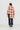 A model is shown from the back wearing a cream and red-orange checkered knit cardigan, and matching scarf with navy blue pinstriped trousers, and dark green socks against a plain white studio background.