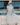 A model wearing a white dress with blue flowers sitting on a boat. 