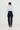 A model shown from the back wearing a light blue long-sleeve button-up shirt tucked into dark navy high-waisted straight-leg jeans, paired with a dark brown beanie and brown leather shoes, against a plain white studio background.