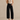 Woman wearing a beige sleeveless top and black high-waisted jeans against a beige background