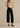 Woman wearing a beige sleeveless top and black high-waisted jeans against a beige background