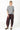 A woman modeling a loose-fit outfit consisting of a gray and white horizontally striped short-sleeve top and dark burgundy baggy pants, paired with dark brown shoes, against a plain white studio background.