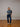 Person wearing a patterned sweater and jeans standing in a room with wooden floor and white walls.