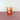 A bright orange striped tumbler on a pink surface with a white background