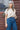 A woman wearing a cream knit top with jeans with a wood background