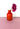 A red vase with a flower on a pink surface with a white background