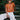 A model wearing an orange top with embroidered white flowers and striped pants sitting on steps. 